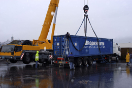 The container is lifted off the truckbed by crane.