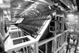 The MINOS neutrino detector in Soudan, Minnesota will consist of 485 layers, each one and half inches thick and weighing 12 tons. Technicians like Dan Marolt (left) erect the planes by clamping them to an iron frame. From a bucket lift, technician Brian LaFrenier, University of Minnesota, checks the placement of plane 393 and releases one of the clamps. The MINOS experiment will measure the oscillation properties of a muon neutrino beam produced by accelerators at Fermilab.